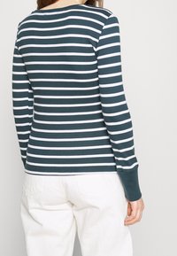 Mörkgrön och vit randig långärmad topp. Har rundad halsringning, åtsittande ärmar och rak fåll. Mjukt bomullsmaterial.