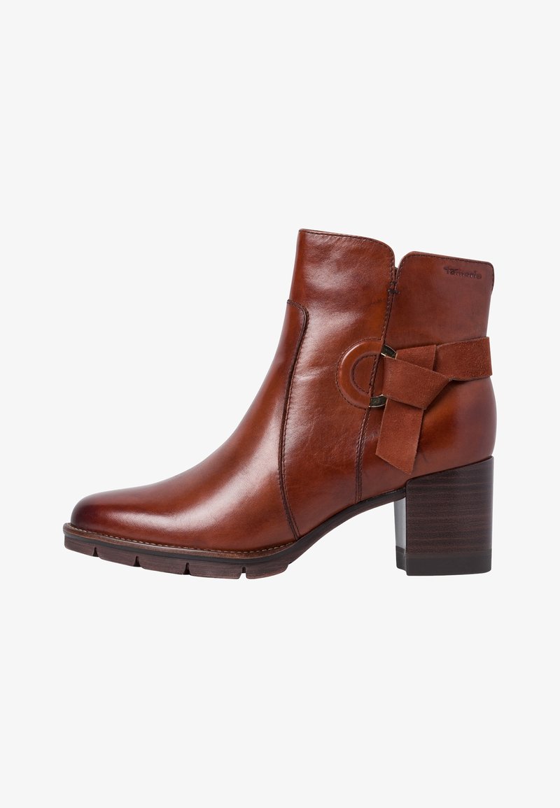 Bottine en cuir marron avec un bout rond, accentuée par un nœud décoratif noué et un talon épais empilé. Texture lisse, design élégant.