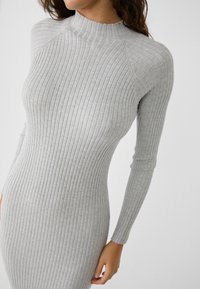 Abito lungo a maniche lunghe grigio a coste con colletto alto, caratterizzato da strisce verticali e una silhouette aderente. Tessuto a maglia morbido e dalla texture piacevole.