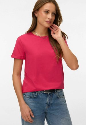 Woman with long brown hair wearing a bright pink short-sleeve shirt, blue jeans with black belt, silver necklace and hoop earrings.