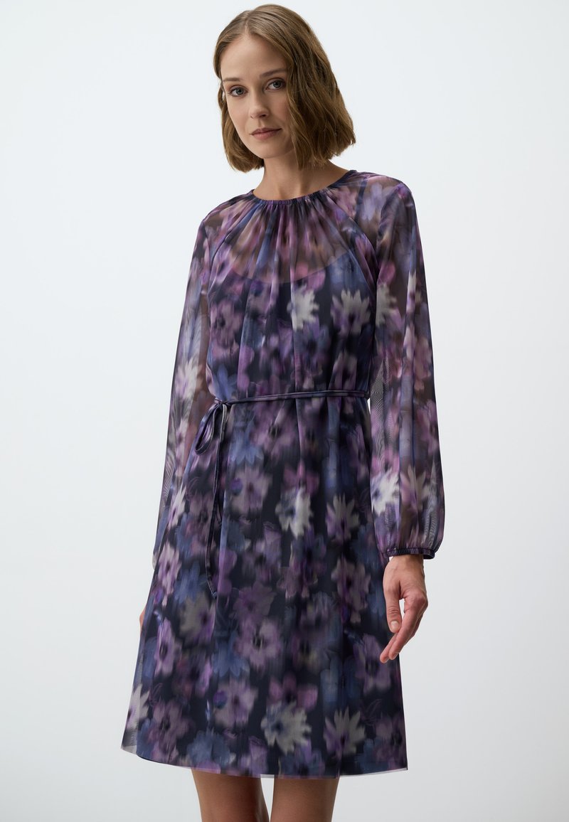 Bloemenprint jurk van doorschijnende stof, met tinten paars en blauw. Lange mouwen, ronde halslijn en een stoffen riem in de taille.