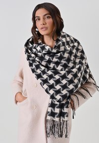 Zwarte en crèmekleurige houndstooth en geblokte sjaal van zacht fabric, met franjes aan de randen; over een lichtroze jas gedrapeerd.