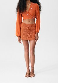 Orange cropped wrap-top med blommig broderi, tillsammans med en virkade minikjol med dragsko i midjan. Bruna sandaler med remmar fulländar looken.