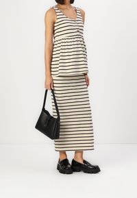 Striped tank top in beige and black, featuring buttons and a gathered waist, paired with a matching striped skirt and chunky black loafers.