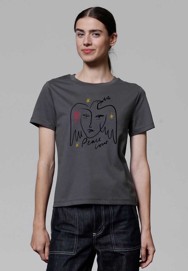 Grijze katoenen t-shirt met een zwart lijntekening van twee gezichten, een rode hart, en de tekst "Peace love", met gele steraccenten. Korte mouwen.