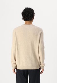 Beige pulóver puha anyagból, kerek nyakkivágással, hosszú ujjal, bordás mandzsettával és aljjal. Simított textúra és laza szabás.