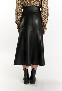 Zwarte leren midi-rok met een strakke taille, met een gladde textuur en paneelontwerp. Gestyled met zwarte enkellaarsjes en een gebloemd blouse.