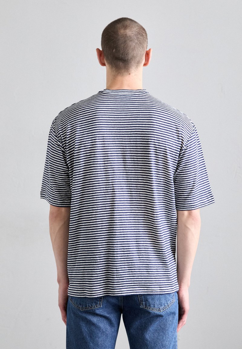 Tricou din bumbac cu dungi, cu o croială lejeră, având dungi orizontale albastre și albe, mâneci scurte și guler rotund.