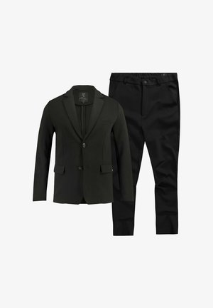 Blazer verde scuro con revers a punta e due bottoni, abbinato a pantaloni neri con vita elasticizzata. Tessuto liscio e sartoriale con tasche.