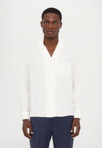 Cămașă albă cu mâneci lungi, cu nasturi, confecționată dintr-un material neted, având un singur buzunar, guler în formă de notch și croială clasică. Pur și simplu cu pantaloni bleumarin.