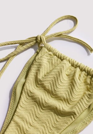 Parte inferior de bikini verde claro con textura y lazos ajustables en los laterales, exhibida sobre un fondo blanco liso.