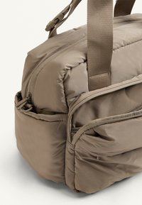 Zaino khaki realizzato in tessuto imbottito, dotato di doppie cerniere, spallacci regolabili e tasche esterne per un ulteriore spazio di archiviazione.