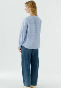 Hellblaues langärmliges Hemd mit roten Tupfen, lockere Passform, geraffter Kragen, elastische Bündchen, kombiniert mit locker sitzenden Jeans.