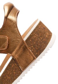 Metallic bronze wedge sandal with cork platform and white ridged sole, featuring a wide strap and heel support with a Velcro closure.