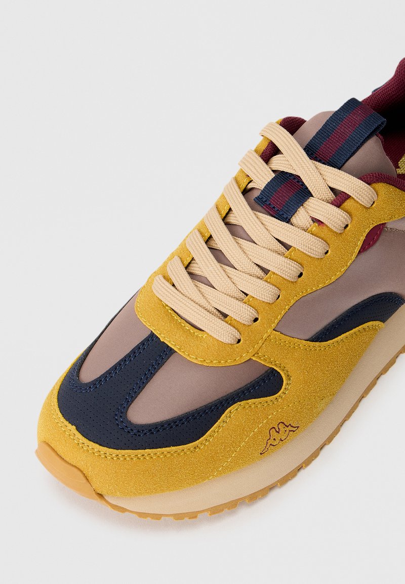 Sneaker con tomaia in camoscio giallo, dettagli navy e pannelli in rete. Presenta lacci beige, logo brandizzato e suola in gomma testurizzata.