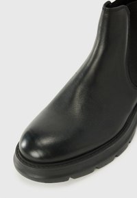 Bottine en cuir noir avec une finition lisse, un bout rond et des panneaux latéraux en élastique texturé. Elle possède une semelle en caoutchouc épaisse pour le confort.
