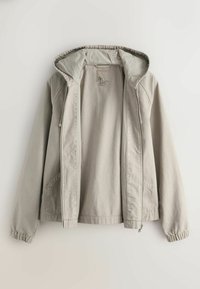 Veste à capuche beige clair avec fermeture éclair, poignets élastiques et poches avant, présentée ouverte sur un fond uni.