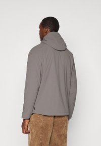 Veste à capuche grise avec une texture lisse et des détails de couture subtils, associée à un pantalon en velours côtelé marron clair.