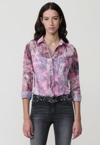 Blusa de manga larga, con estampado rosa de patrones variados de animales, cuello tipo camisa y puños remangados. Combinada con jeans oscuros y un cinturón de piel de serpiente.