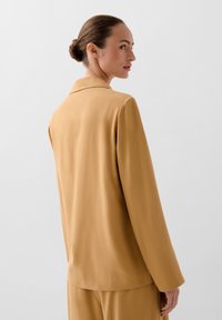 Senfgelber Blazer mit glatter Textur, einreihigem Design und abgesetztem Kragen, von hinten vor einem neutralen Hintergrund präsentiert.