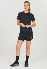 Zwarte sport T-shirt en shorts, met een gladde textuur en een logo op de shorts. Draag het met zwarte sokken en hardloopschoenen.