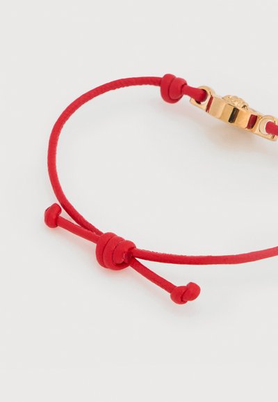 Βραχιόλι με κόκκινο κορδόνι, ρυθμιζόμενο κλείσιμο με ολισθαίνουσα θηλιά και μεταλλική χρυσή λεπτομέρεια, με απαλό υλικό και μινιμαλιστικό σχεδιασμό.
