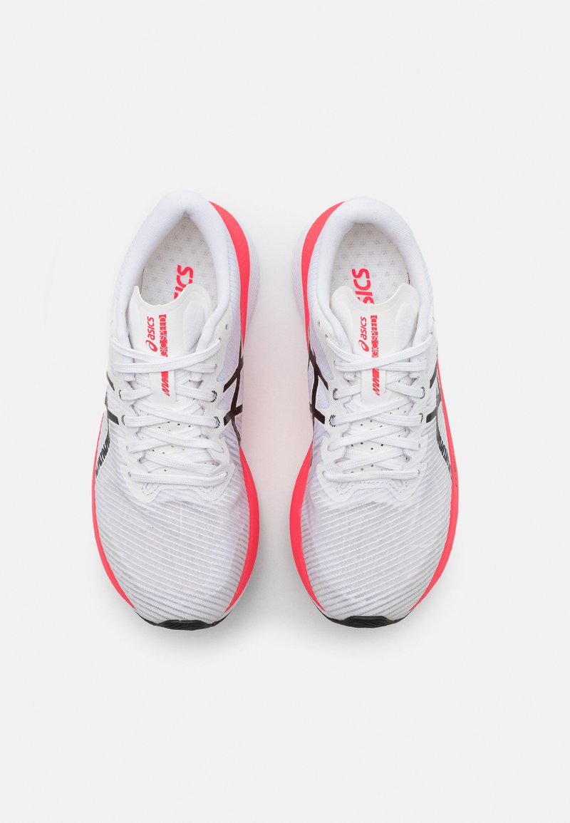 Baskets de sport blanches avec des accents roses, présentant une tige texturée, des lacets plats et un logo noir sur le côté.