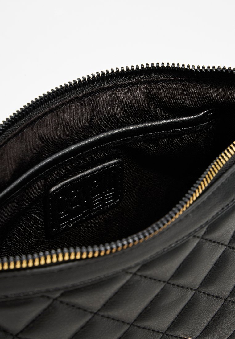 Pochette in pelle trapuntata nera con zip dorata e rivestimento interno nero. L'interno presenta un'etichetta e una tasca sottile su una texture liscia.