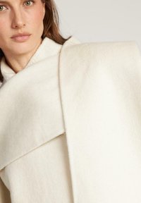 Cappotto bianco in lana con una texture liscia, un ampio colletto e un design sovrapposto, ideale per essere stratificato durante il tempo fresco.