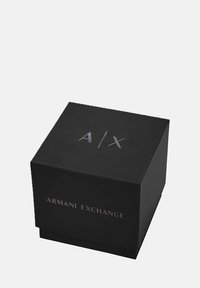 Čierna štvorecová darčeková krabička s matným povrchom, s embosovaným strieborným logom "A/X" na vrchu a nápisom "ARMANI EXCHANGE" na prednej strane.