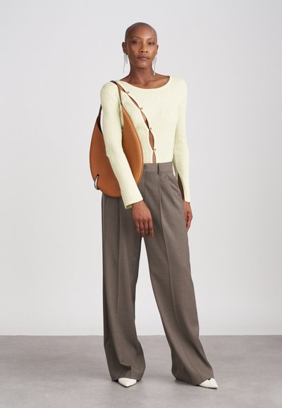 Gai zaļš ribotais garo piedurkņu tops ar pogu detaļām, kombinēts ar pelēkām brīvām biksēm un brūnu ādas plecu somu.