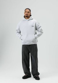 Lichtgrijze capuchonsweatshirt met "ZERO" in het zwart op de voorkant, gecombineerd met oversized zwarte spijkerbroek en zwarte veterschoenen.