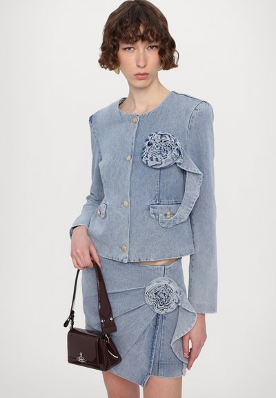 Hellblaue Jeansjacke mit Blumenapplikationen und goldenen Knöpfen, kombiniert mit einem Jeansrock mit Raffung und ähnlichen Blumendetails.
