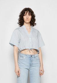 Camisa azul-clara, corta, com botões, mangas curtas e riscas brancas verticais; apresenta um laço na bainha e um colarinho mandarin.