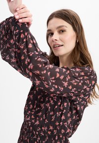 Schwarzes Blumenkleid mit kleinen roten und rosa Mustern, langen Puffärmeln und gerafftem Bauch. Aus einem leichten, durchsichtigen Stoff gefertigt.