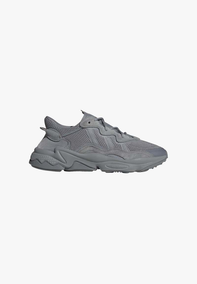 Scarpe da ginnastica grigie realizzate con materiali in rete e suede. Presentano una suola testurizzata, un design con lacci e una forma ergonomica. Vista laterale mostrata.