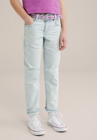 Ljusblå jeans med slitna knän och avslappnad passform, matchade med ett lavendelfärgat bälte med silverdetaljer och vita sneakers.