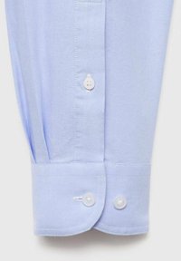 Puño de camisa de algodón azul claro con dos botones blancos, que presenta una textura suave y un dobladillo redondeado, con sutiles detalles de costura.