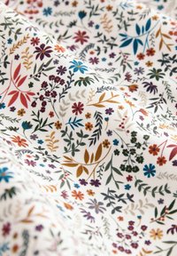 Tissu en coton avec un fond blanc présentant des motifs floraux et de feuilles multicolores dans des teintes de violet, bleu, vert et orange.