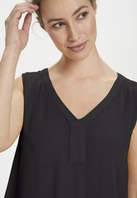 Haut sans manches noir avec un décolleté en V et une finition texturée, présentant un détail de couture subtil à l'avant et des emmanchures lisses.