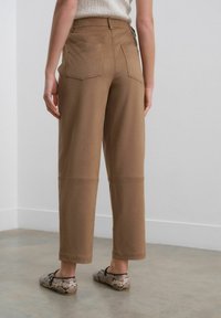 Brune bomulds cargo bukser med en afslappet pasform, har to baglommer og detaljerne ved knæsaumen. Mønstret sko fuldender outfittet.