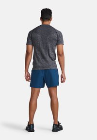 Grå kortärmad träningsskjorta i kombination med blå shorts och svarta sneakers. Tyget ser strukturerat och andningsbart ut, designat för aktiv användning.