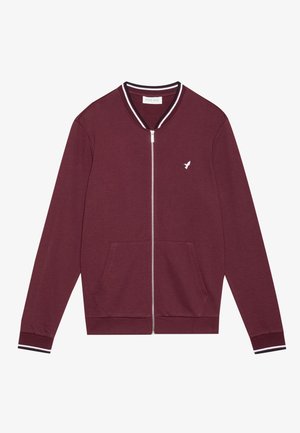 Burgundska jakna na zip s bijelim grbom, rebrastim ovratnikom i manžetama s crno-bijelim prugama, te dva prednja džepa.