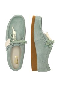 Helle grüne Wildlederschuhe mit runder Form, ausgestattet mit einer Schnürung und einer strukturierten, tanfarbenen Gummisohle. Logo an der Seite.