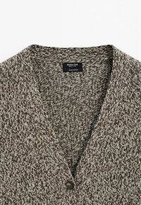 Brązowy i kremowy sweter o dzianinowym splocie, 100% bawełna, z dekoltem w kształcie litery V, pojedynczym zapięciem na guzik oraz teksturowanym wzorem. Metka widoczna wewnątrz.