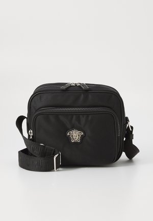 Bolso bandolera de nylon negro con un bolsillo frontal con cremallera, herrajes plateados y logo de Medusa. Cuenta con una correa de tela ajustable y forma rectangular.