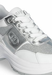 Sneaker bianca con accenti argentati, caratterizzata da una parte superiore testurizzata, un design con lacci, dettaglio del logo e una suola spessa per un'altezza aggiuntiva.