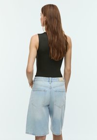 Črna brezrokavnica v kombinaciji s svetlo modrimi jeans kratkimi hlačami. Kratke hlače so z visokim pasom, zrahljanimi robovi in zadnjimi žepi.