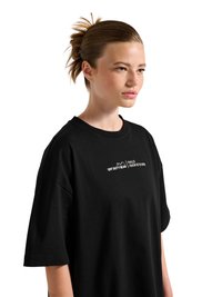 Młoda kobieta z włosami związanymi do tyłu, ubrana w luźną czarną koszulkę z białym napisem „OFF DUTY GEAR HALO” na piersi, zwrócona w prawo.