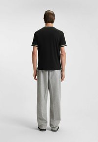 Sort kortærmet t-shirt med grøn kant, parret med lysegrå bredbenede bukser. Blødt materiale med en afslappet pasform og minimalistisk design.